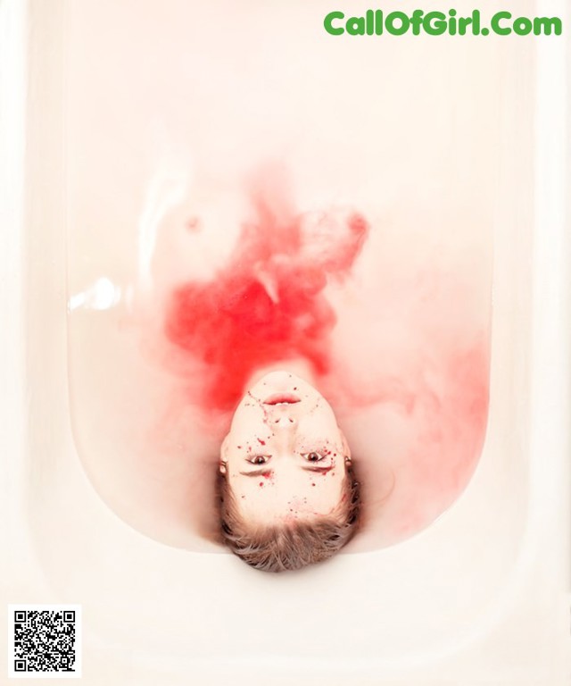 A woman in a bathtub with blood on her face.