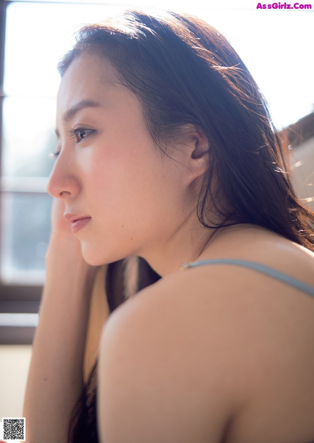 A woman sitting in front of a window with her hand on her chin.