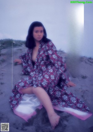 A naked woman sitting on top of a bed next to a window.