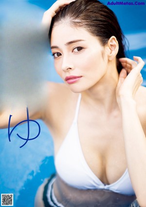 A woman in a white bikini sitting on the edge of a swimming pool.