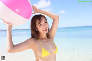 A woman in a yellow bikini posing on a beach.