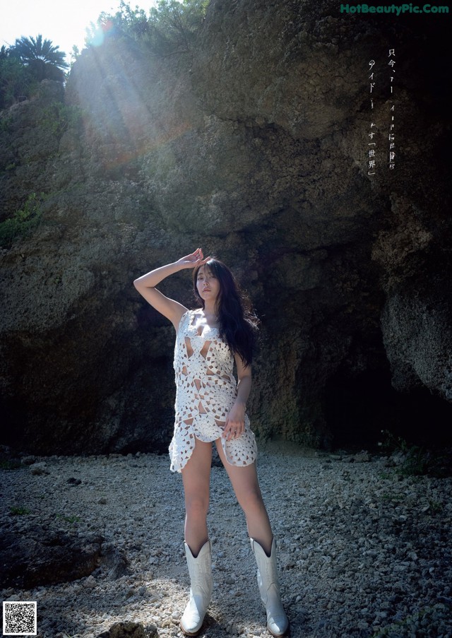 A woman in a white dress and cowboy boots posing for a picture.