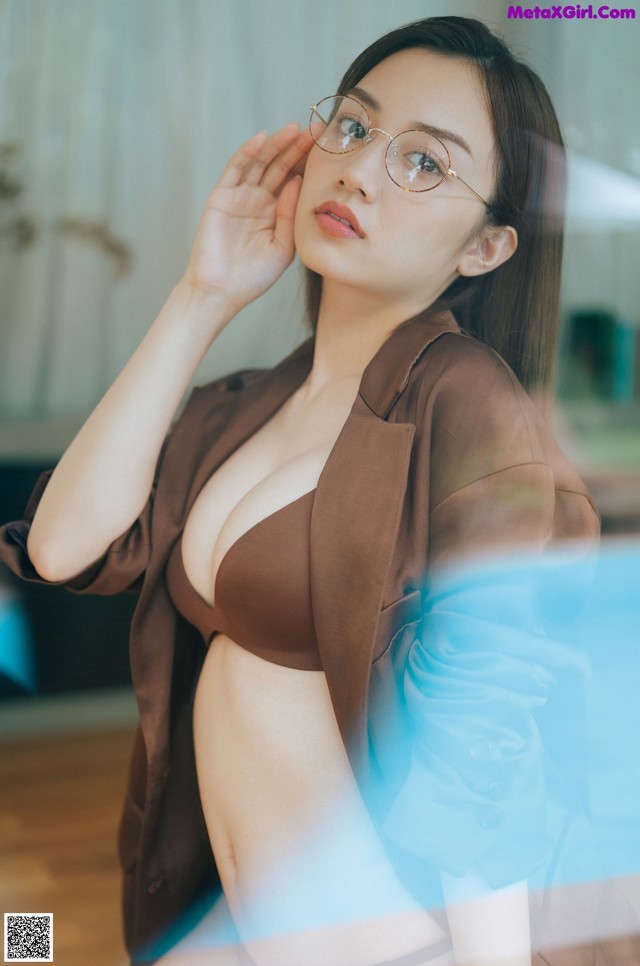 A woman wearing glasses sitting on a wooden floor.