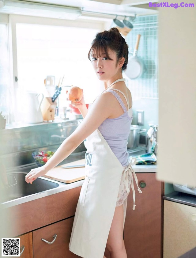 A woman in an apron standing in a kitchen holding an apple.