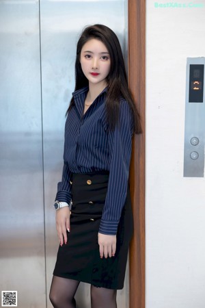 A woman in a black skirt and stockings leaning against an elevator.