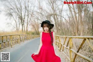 A woman in a red dress and black hat posing for a picture.