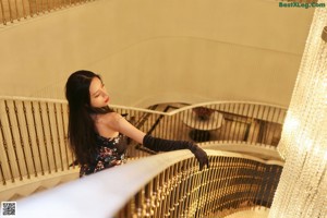 A woman in a black dress and gloves standing on a staircase.
