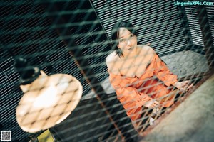 A woman sitting on a chair in an orange jumpsuit.