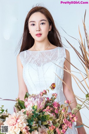 A woman in a white dress sitting on a chair next to flowers.