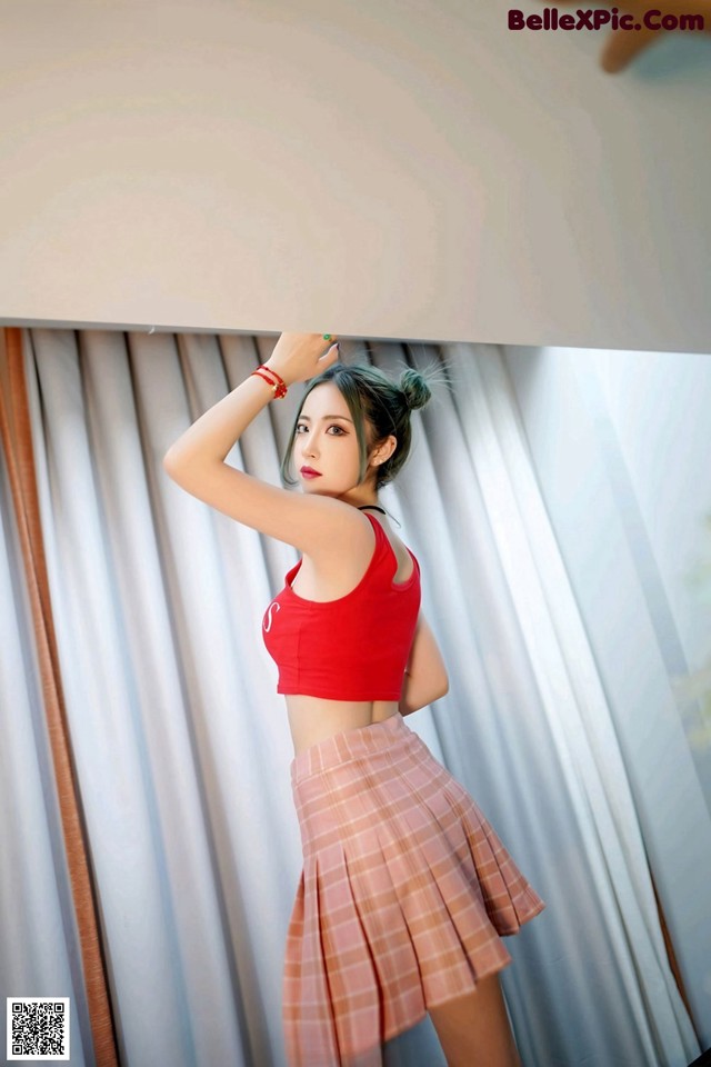 A woman in a red top and plaid skirt posing for a picture.