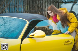 A woman in a yellow jacket leaning out the window of a yellow car.