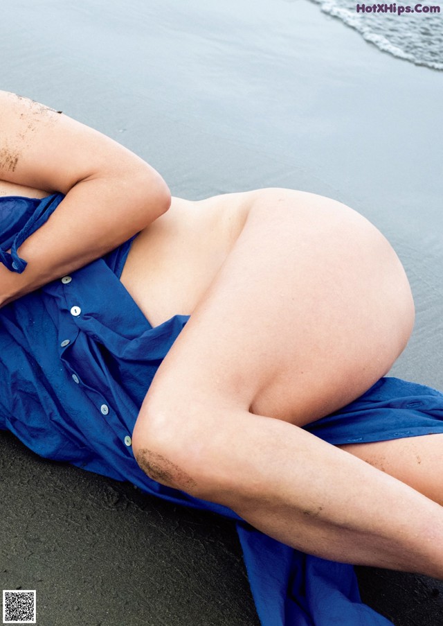 A woman in a blue dress laying on the beach.