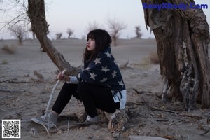 A woman wrapped in a blanket sitting in the sand.