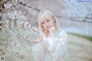 A little girl in a white dress is standing under a tree.