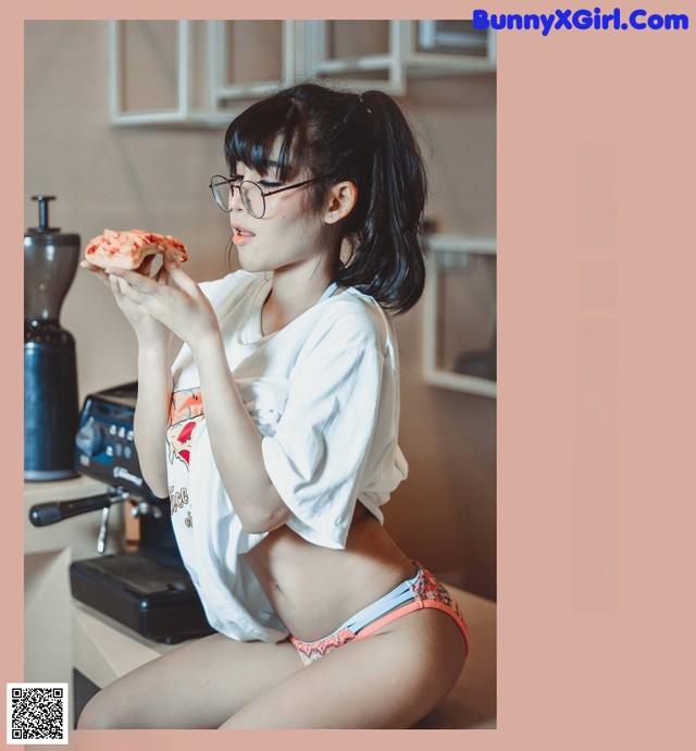 A woman in a white shirt and pink panties eating a piece of pizza.