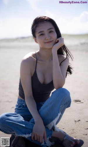 A woman sitting on the beach with her hand on her chin.