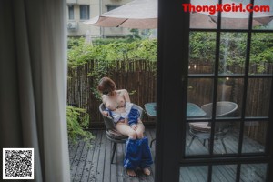 A naked woman sitting on a chair under an umbrella.