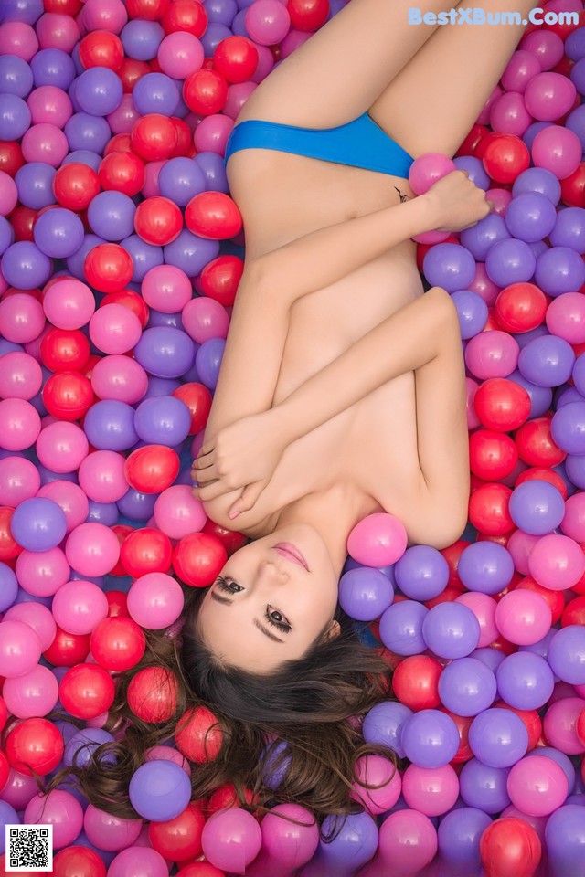 A woman in a blue bikini laying in a ball pit.