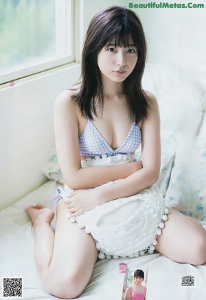 A woman in a blue and white bikini sitting on a bed.