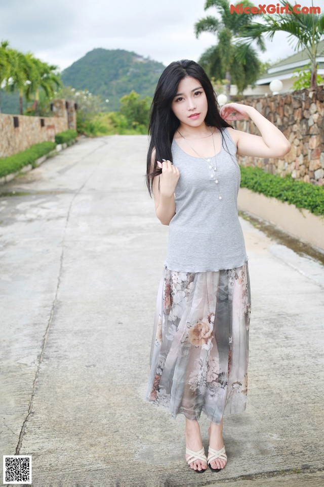 A woman in a gray tank top and floral skirt posing for a picture.