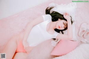 A woman in a white top and pink panties sitting on a bed.