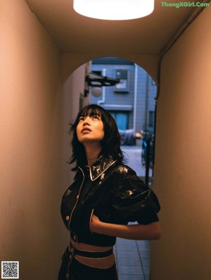 A woman leaning against a wall in a black and gold outfit.