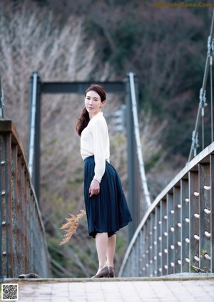 A woman in a white blouse and blue skirt standing on a tatami mat.