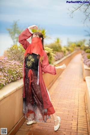 A woman in a red robe leaning against a wall.