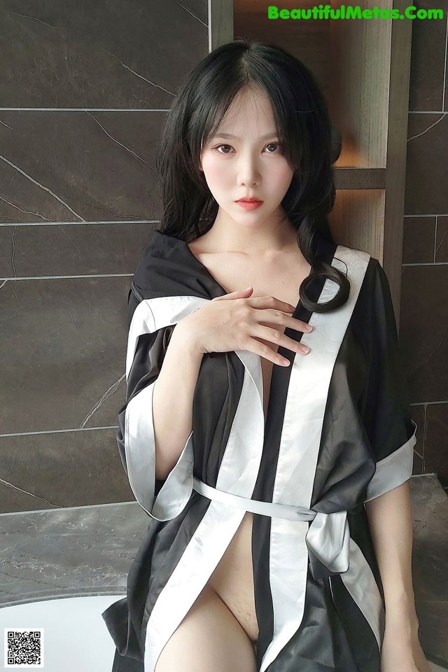A woman in a black and white robe sitting in a bathtub.
